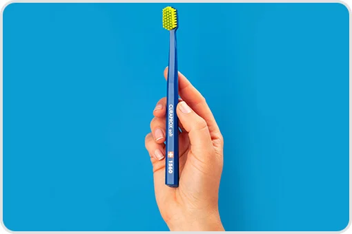Hand holding a Curaprox 1560 blue toothbrush with soft bristles