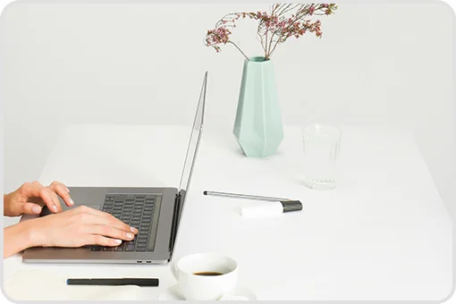 Hands typing on laptop on white desk with coffee and vase, symbolizing to schedule an appointment with a dentist near me in Coyoacan.