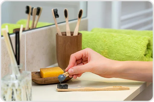 Bamboo toothbrush over sink, with hand applying paste. Illustrative image for dental hygiene myths.