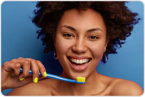 Smiling woman using soft bristle toothbrush in front of blue background